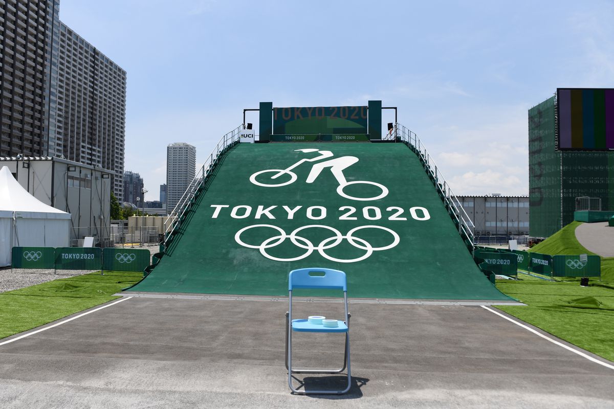 An empty folding chair in front of a ramp with the Tokyo 2020 Olympic rings on the slope.