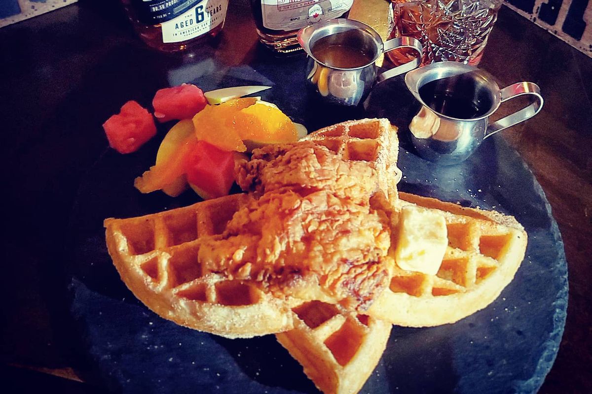 A plate of waffles with chicken with bottles of whiskey behind it