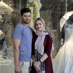 In this July 3, 2019 photo, newly married Iranian couple Mohammad Davoodi, 28, and his wife Mahsa Asadzadeh, 20, pose for a photo in front of a wedding dress shop in downtown Tehran, Iran. Iran’s large middle class has been hit hard by the fallout from unprecedented U.S. sanctions, including the collapse of the national currency. Perhaps most devastating has been the doubling of housing prices. More newlyweds move in with their families to save money. (AP Photo/Ebrahim Noroozi)