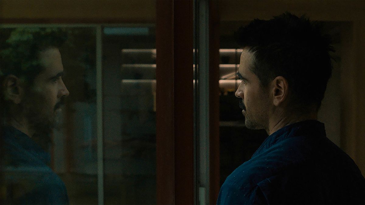 A man looks into a window and sees his reflection.