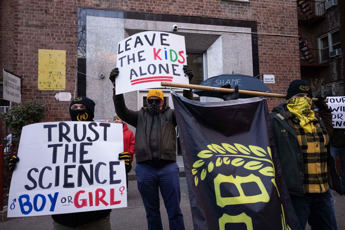 Members of the Proud Boys carry protest signs that read “trust the science, boy or girl” and “Leave the kids alone.”
