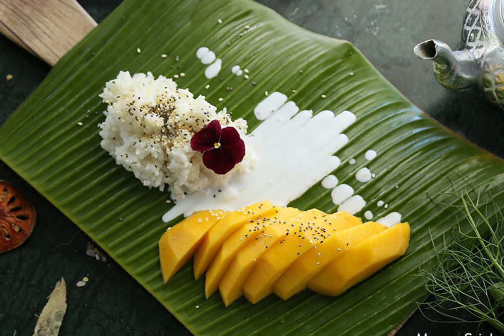 Sticky rice, mango, and coconut milk on a banana leaf. 