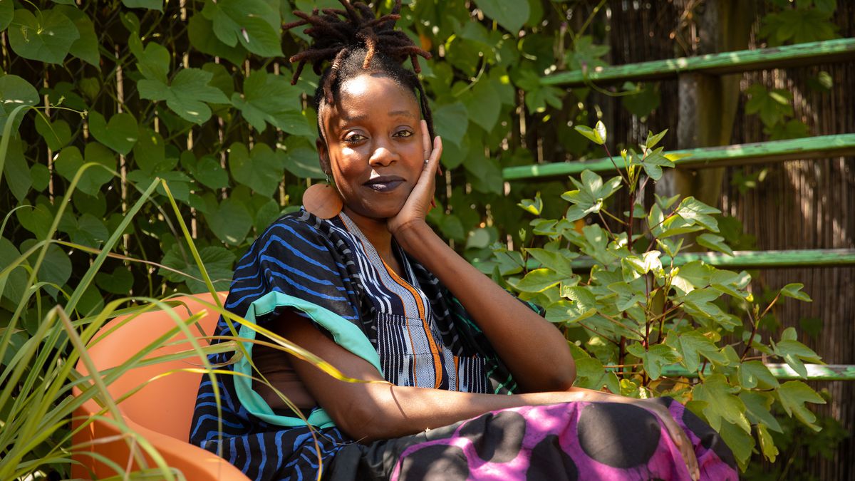 Yewande Komolafe sits in an orange chair, surrounded by plants.
