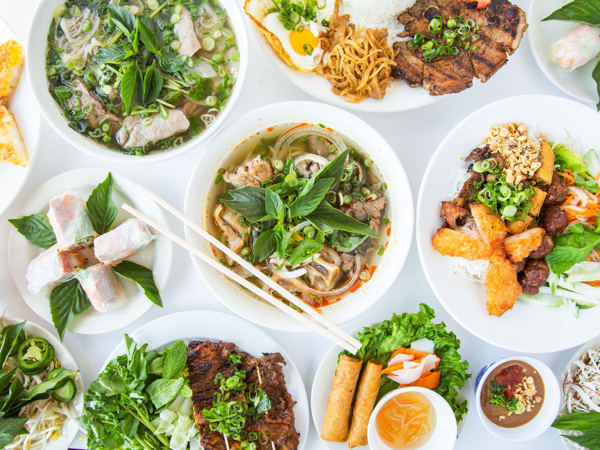 Overhead shot of various Vietnamese dishes, including soups and more, on a white background.
