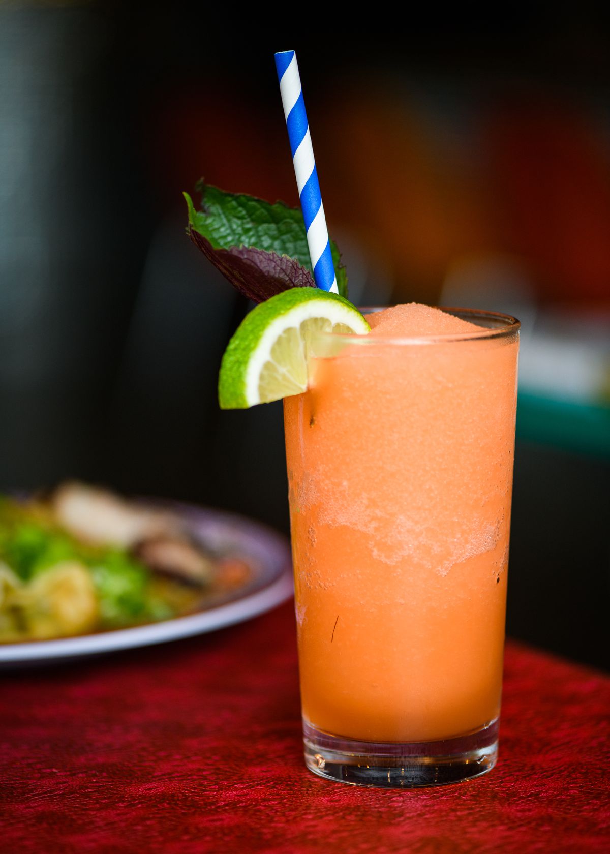 An orange slushie, garnished with a lime, sits on a red table at Oma’s Hideaway. The Moonage Daydream Slushie is made with tequila, pineapple, and mint.