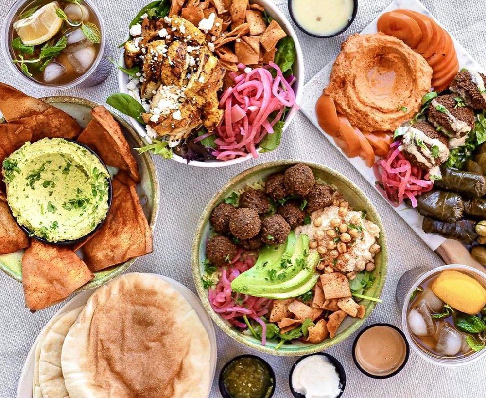 An overhead photo of crispy pita and hummus and grilled meats in bowls.