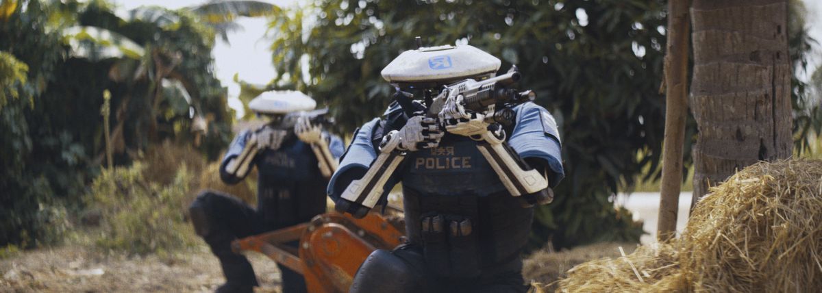 Two robot police officers, crouching in a tropical locale, aim shotguns in The Creator.