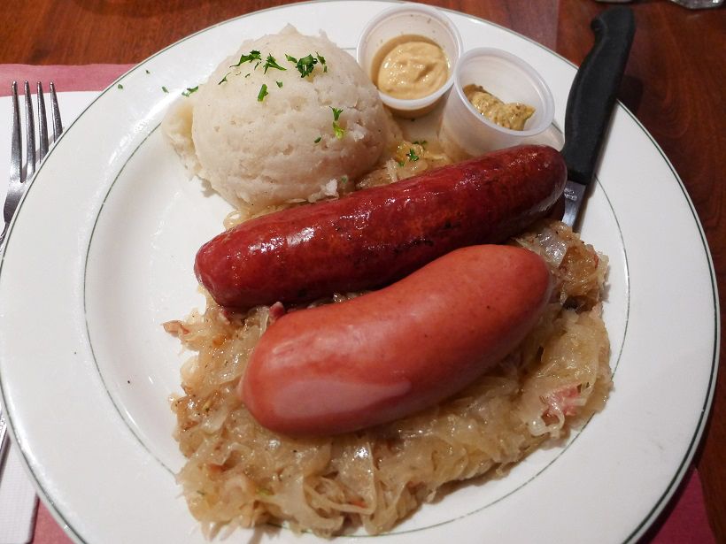 A pair of dissimilar sausages on a bed of sauerkraut with mashed potatoes and mustard on the side.