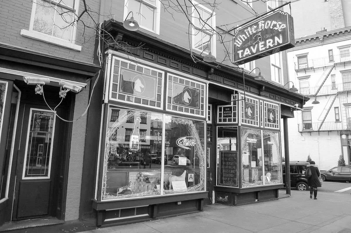 An old facade with horse heads etched in glass and neon tavern sign overhead.