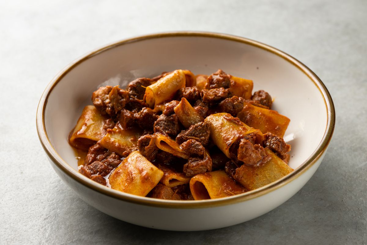 A close up shot of a rigatoni pasta in deep red sauce with cubes of meat.