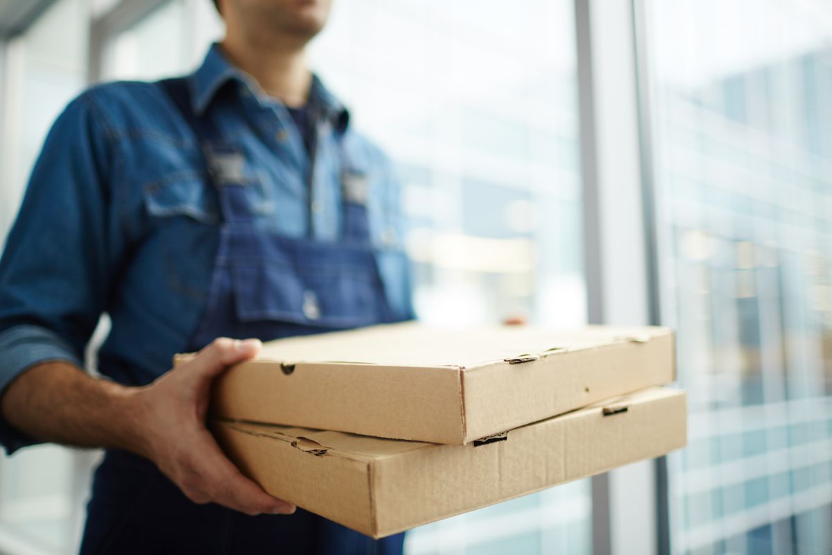 Two boxes with fast food being carried by delivery man in uniform for one of clients 
