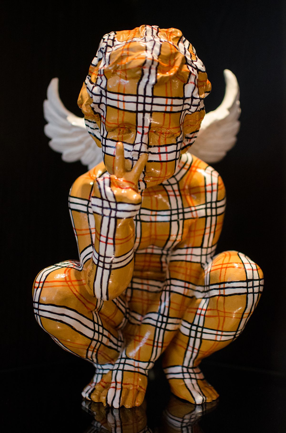 An angel sculpture covered with an orange plaid pattern gives a peace sign.