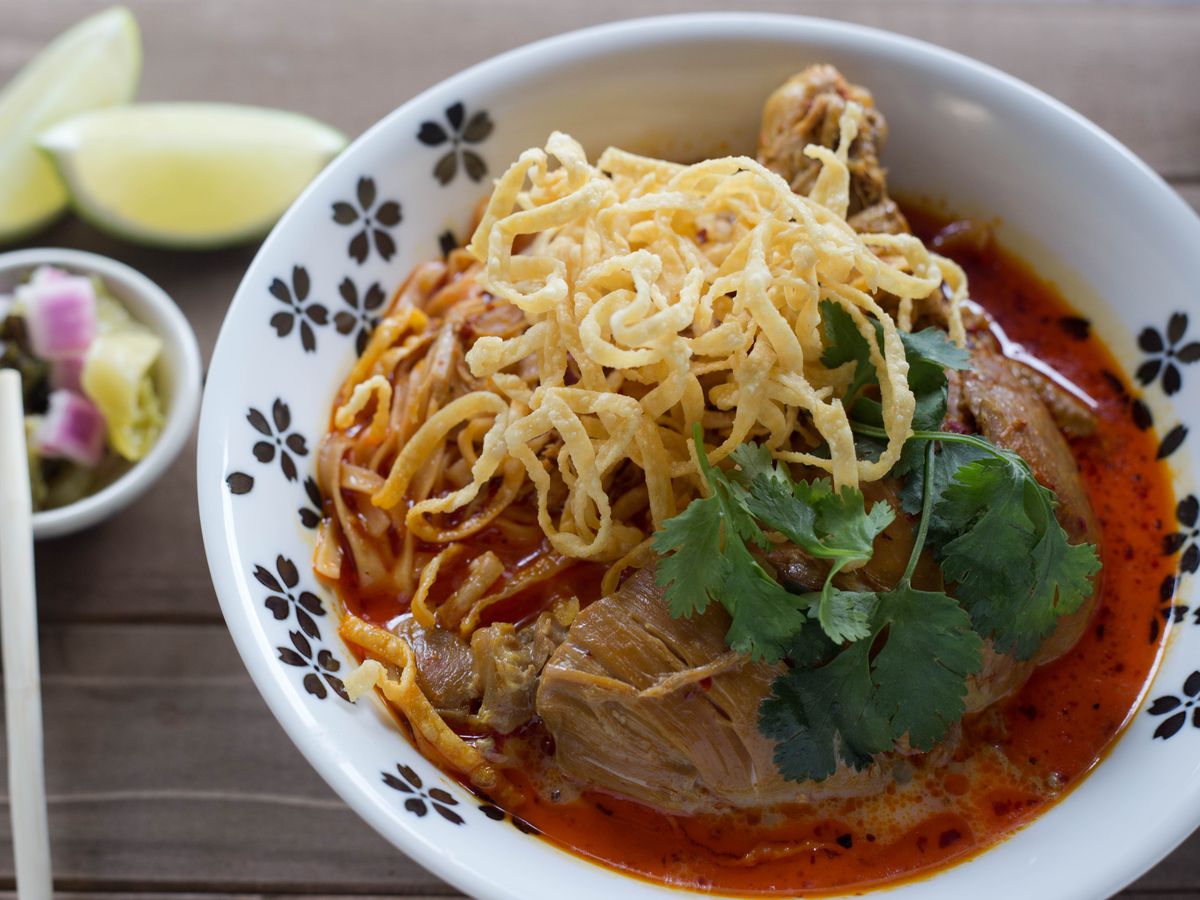 A decorative bowl of khao soi, with pickled vegetables on the side