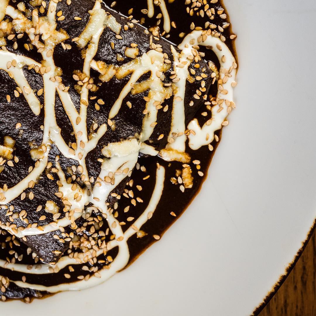a plate of brisket enchiladas covered in black mole and drizzle of white crema and a sprinkle of sesame seeds, all from Mi Vida Mexican restaurant