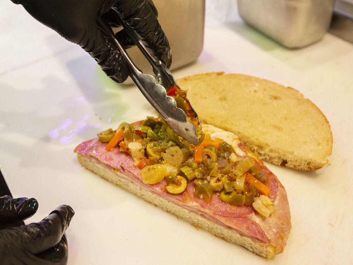 A muffuletta open and being topped.