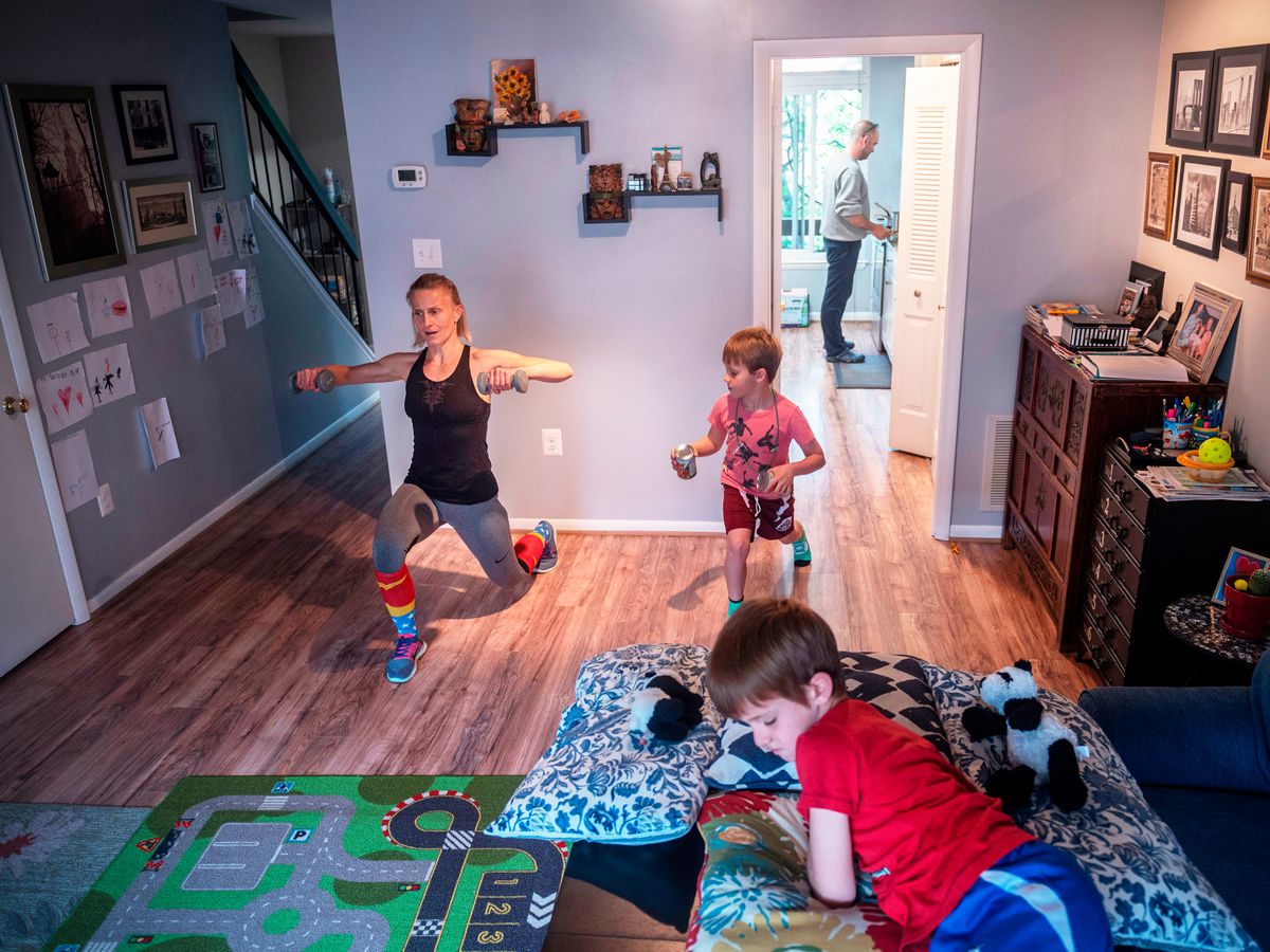 A woman in a yoga pose in her home with her two children and partner visible in the frame.