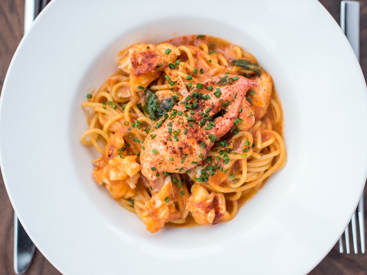 A white bowl filled with spaghetti with red sauce and lobster.
