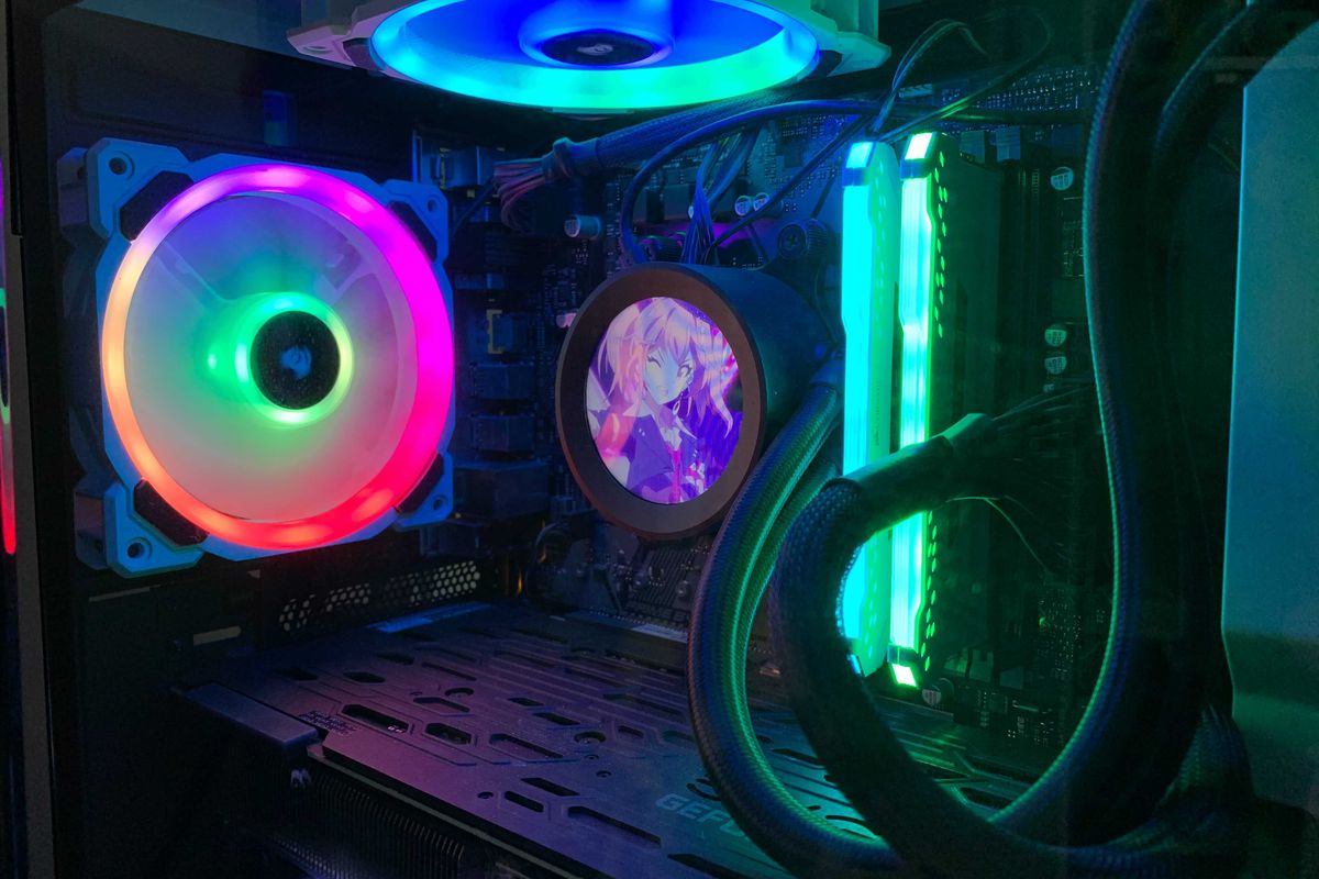 A photo of the inside of a PC case. It’s filled with glowing rainbow components and a tiny LCD screen that shows an anime character with pink hair. 
