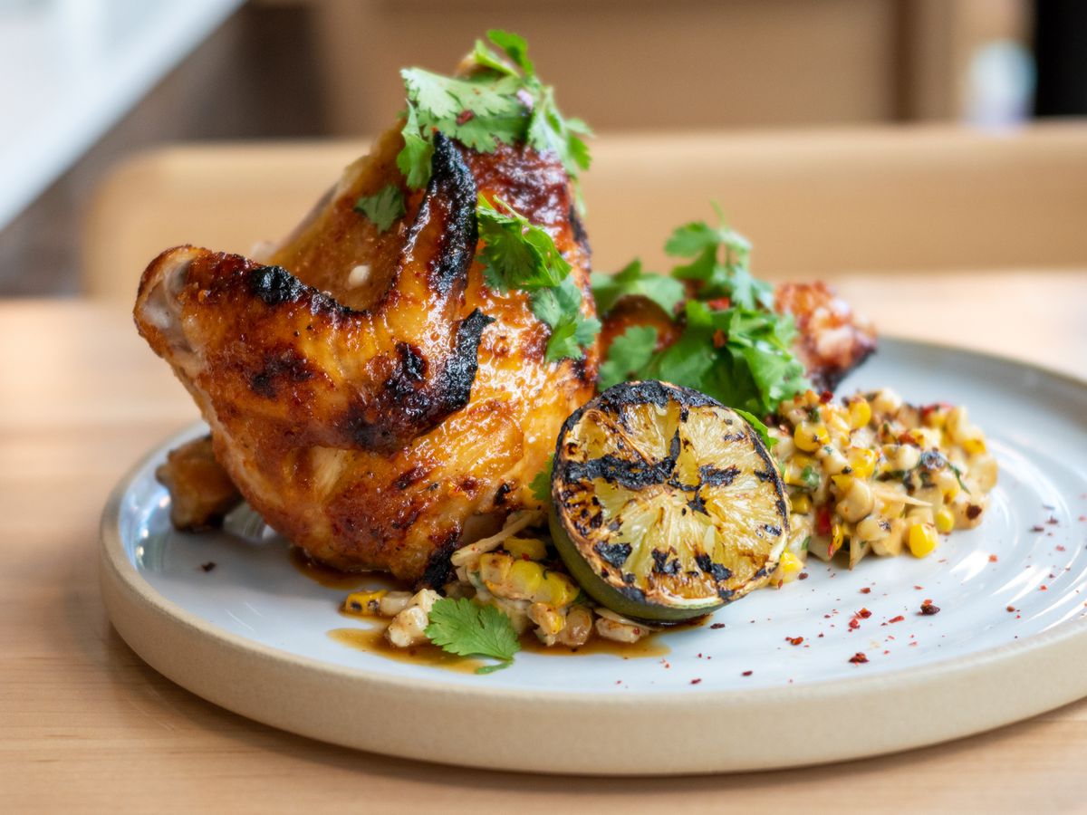A plate of half smoked chicken with grilled lime and corn, drizzled with green herbs.