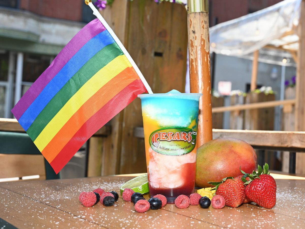 A rainbow margarita in a plastic cup with a Pride flag.
