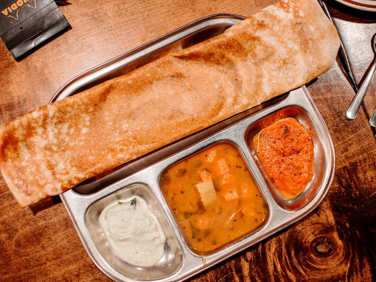A silver tray with a dosa and three kinds of sauce and vegetable curry.