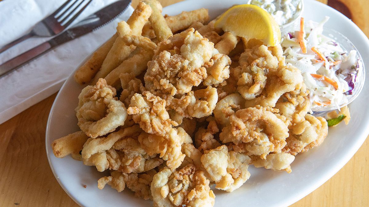 A plate of fried clams, fries, coleslaw, and lemon wedge