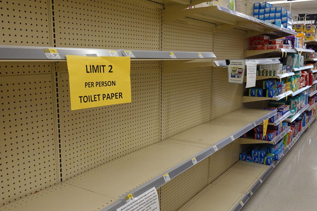 Empty toilet paper shelves in a store, with a “limit 2 per person” sign.