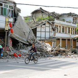In this photo released by China's Xinhua News Agency, a local resident bicycles in front of collapsed houses after an earthquake struck in Lushan County, Ya'an City, in southwest China's Sichuan Province, Saturday, April 20, 2013. A powerful earthquake struck the steep hills of China's southwestern Sichuan province Saturday morning, leaving at least 160 people dead and more than 6,700 injured. 
