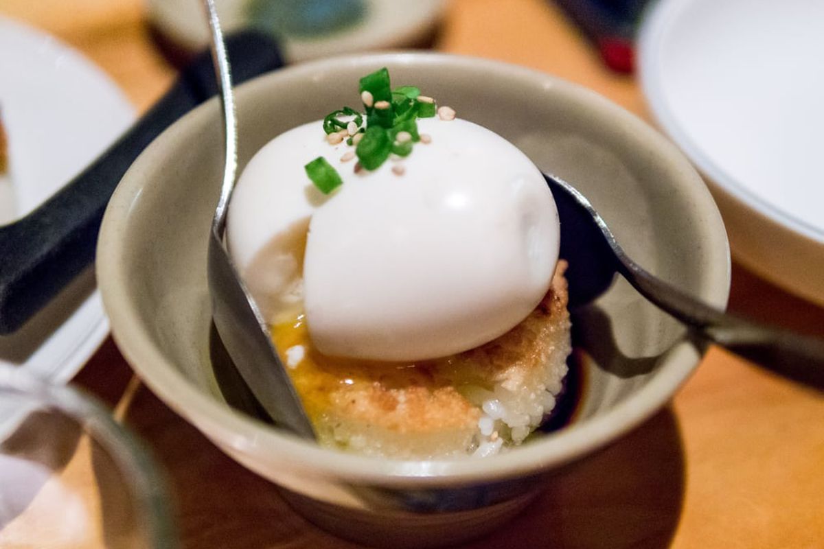 A shot of the shoyu tamago runny egg over crispy rice with two spoons at Ruby Chow’s in Atlanta