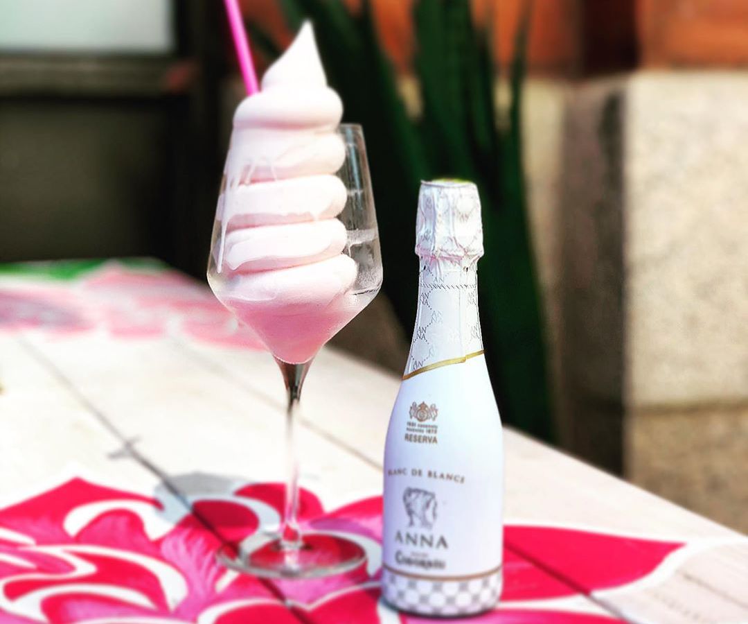 A swirl of pink sorbet is served in a wine glass with a pink twisty straw and sparkling rose poured in the same glass. A small bottle of rose sits next to the glass.