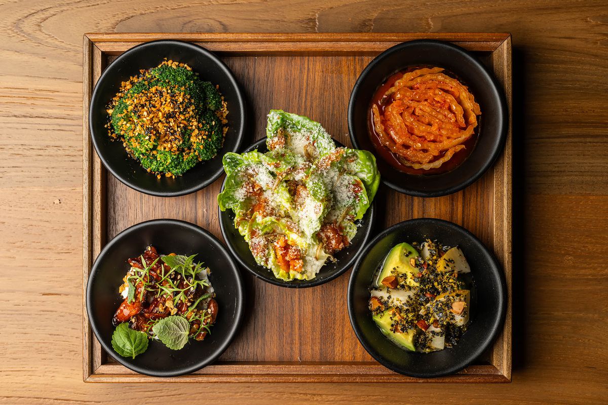 An overhead shot of five black bowls of vegetable snacks on a wooden board at LA restaurant Yangban.