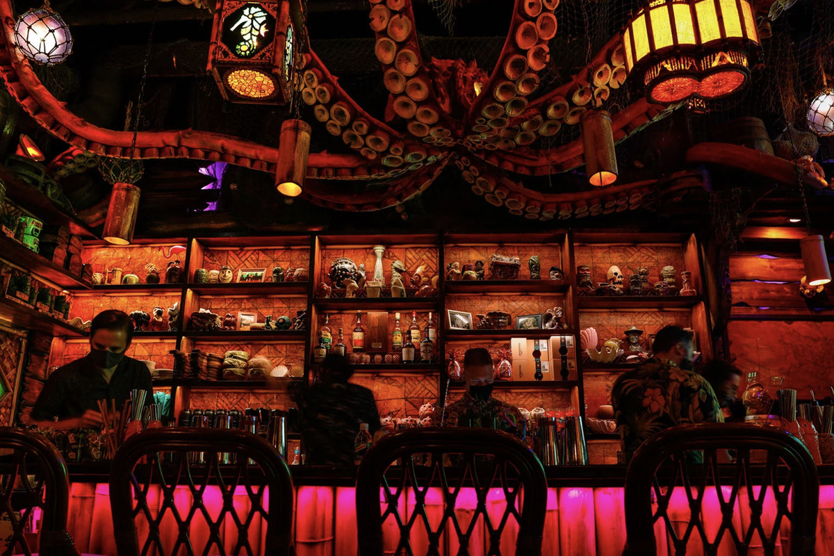 The interior of Capitol Hill bar Inside Passage, with four masked bartenders behind the bar; a giant tentacled octopus is hanging from the ceiling.