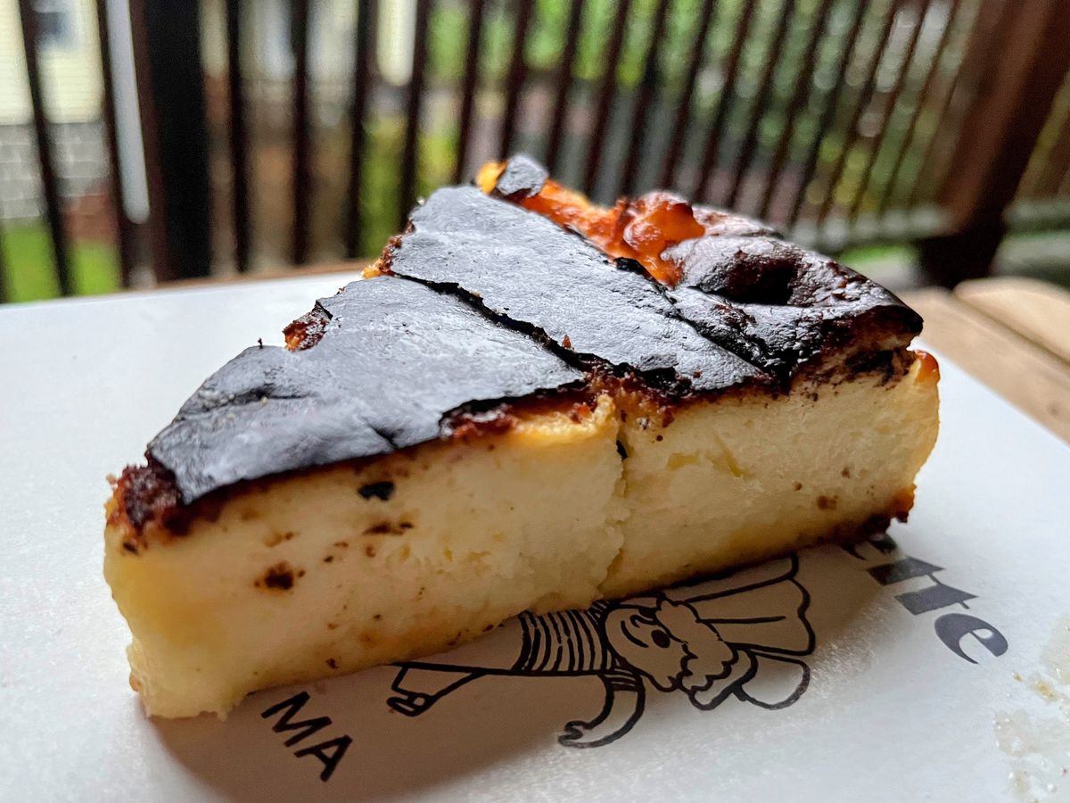 A slice of creamy Basque cheesecake with a burnt, blackened top set on top of a white pastry box.
