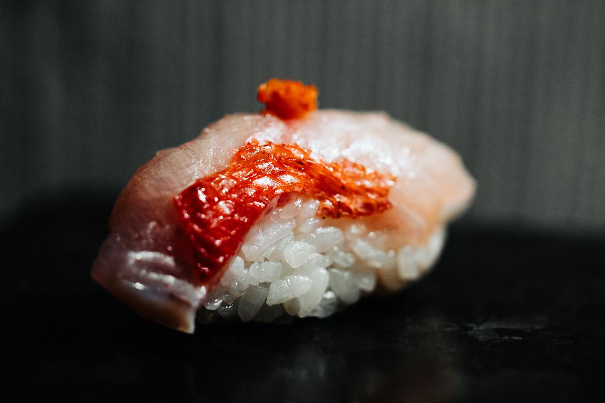 A piece of nigiri made with pink and red fish on top of a clump of white rice.