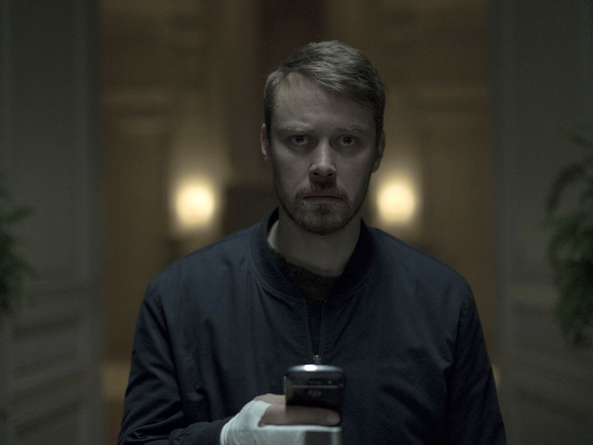 Michael Dorman looks sad while holding a cell phone in Patriot