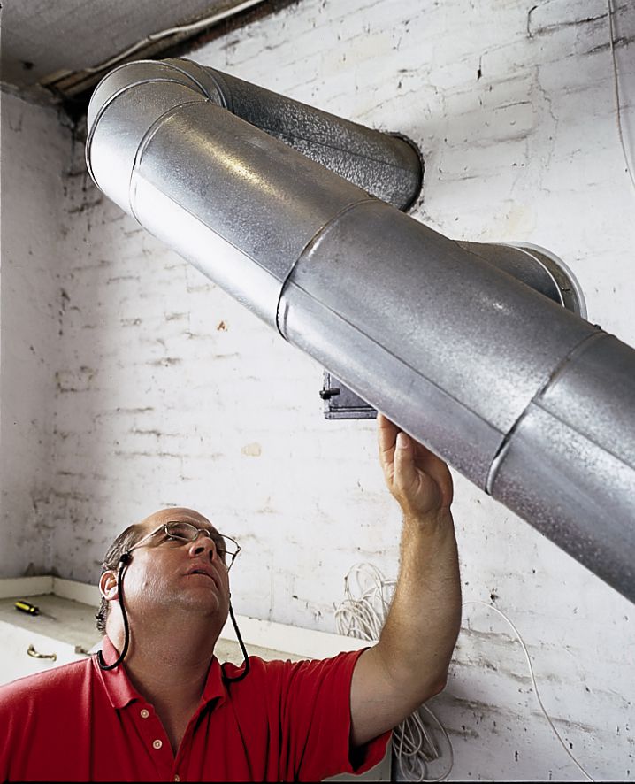 Person inspecting a flue pipe for holes and leaks during for fall furnace maintenance.
