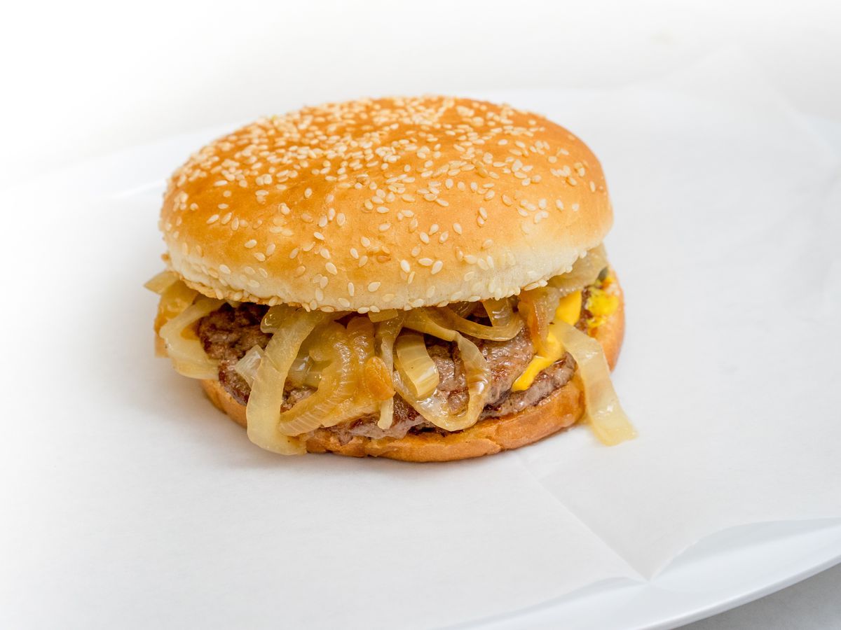 A burger topped with cooked onions on a white table.