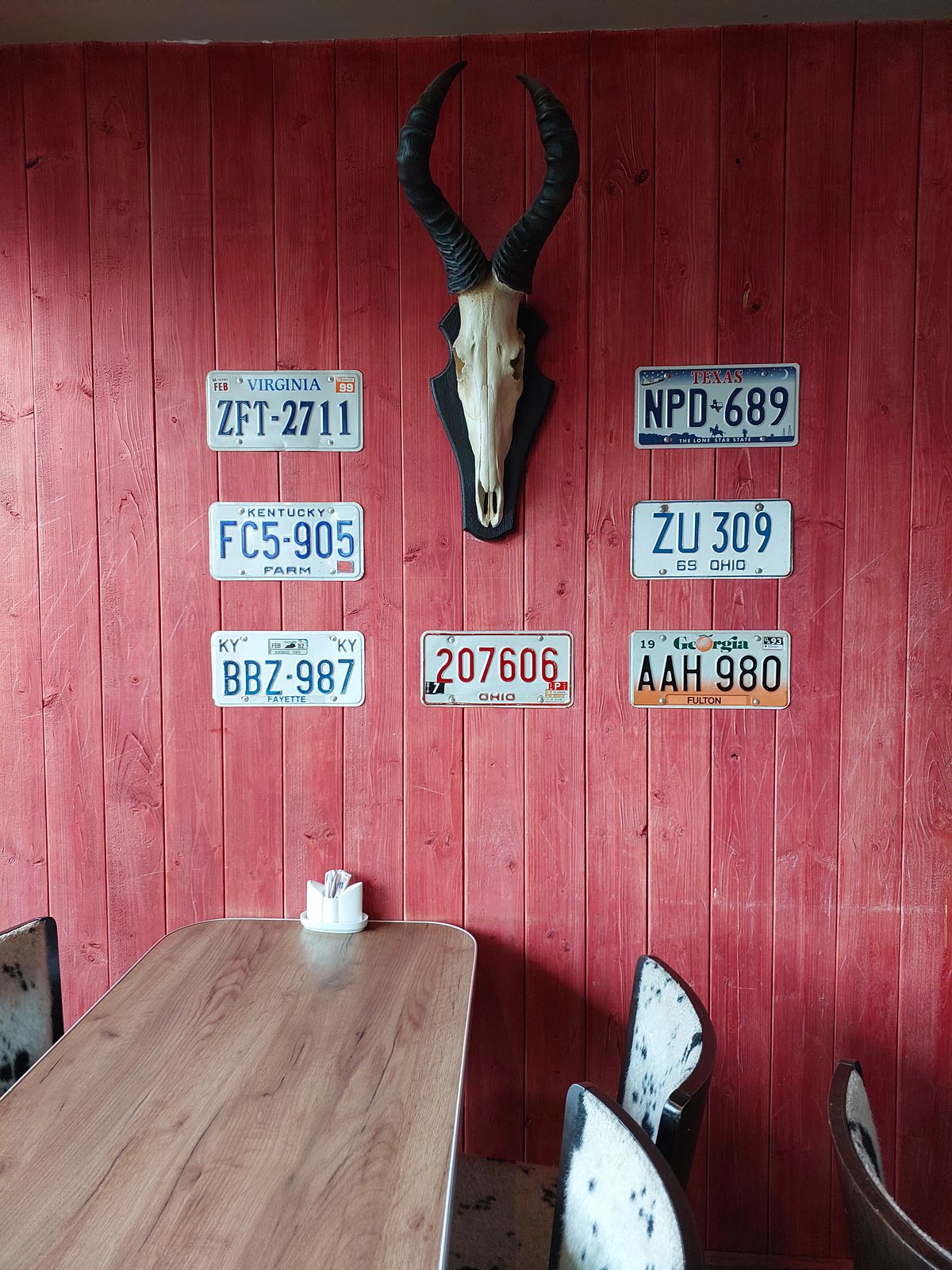 An animal skull hangs among American license plates on a red wood wall.