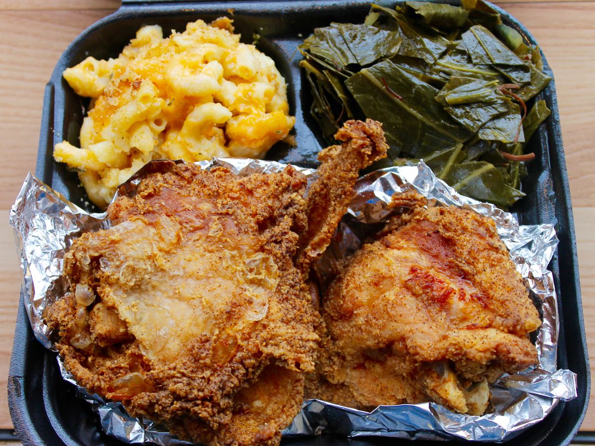Fried chicken plated on foil with sides of mac and cheese and collard greens