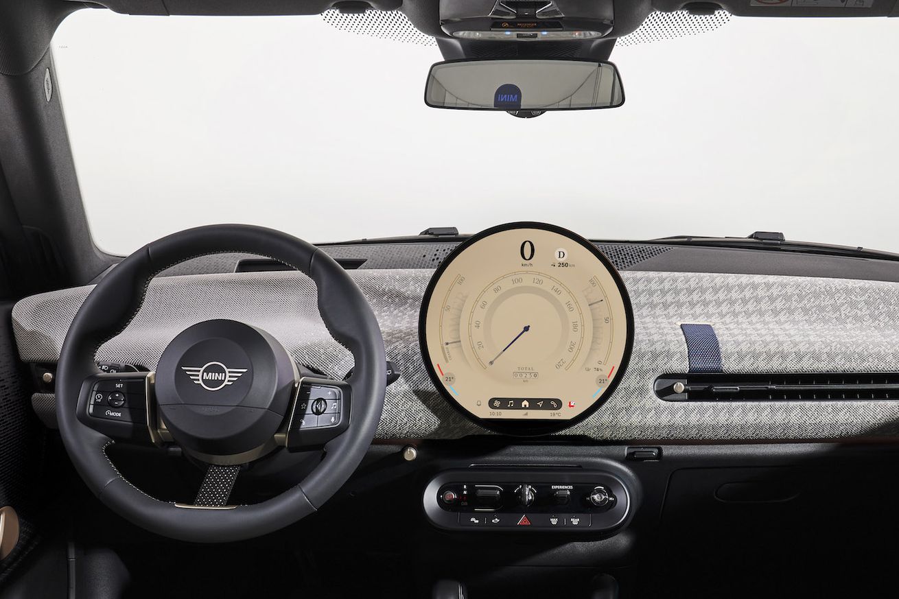 A picture of the interior of the 2025 Mini Cooper, seemingly taken from between the driver and passenger seats. It shows the steering wheel, center OLED screen, and dashboard.