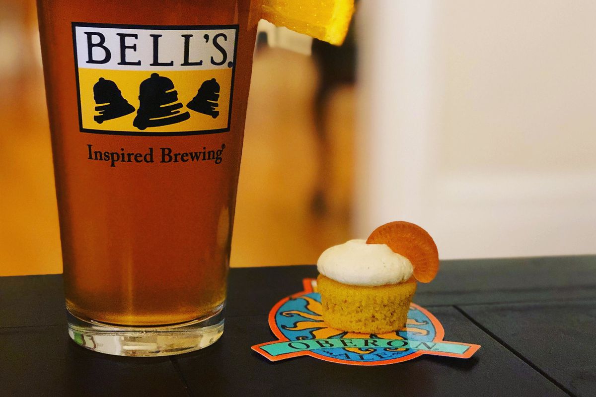 A glass of beer beside a small cupcake.