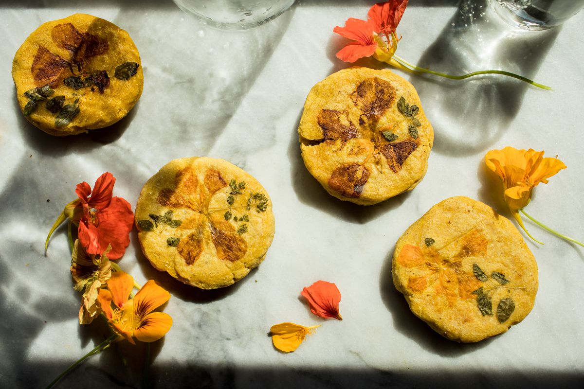 Arepas sit on a marble surface with flowers scattered around them.