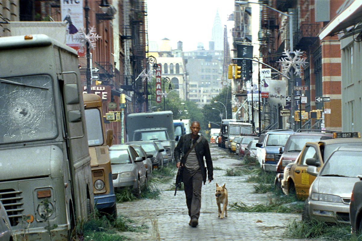 A man (Will Smith) in a dark coat walks through a deserted street lined with abandoned cars beside a dog in I Am Legend
