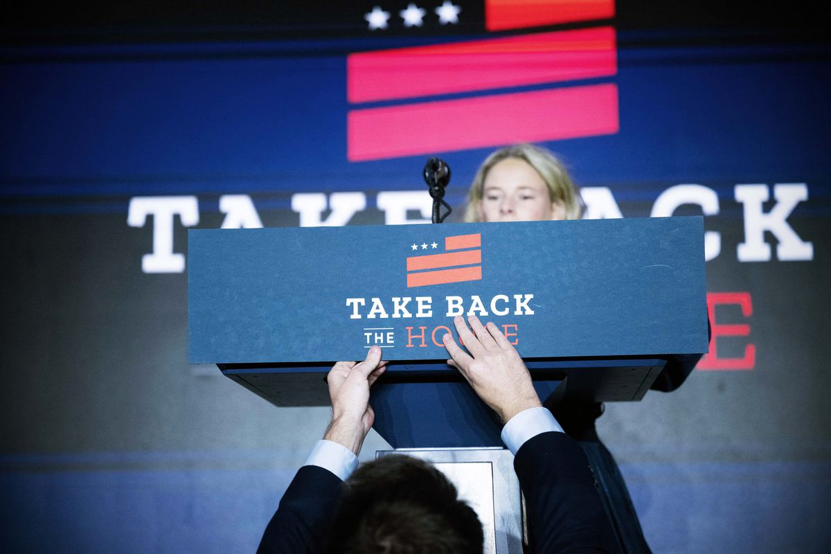 A view of a congressional staffer adhering a sign to a lectern that reads “TAKE BACK THE HOUSE.”