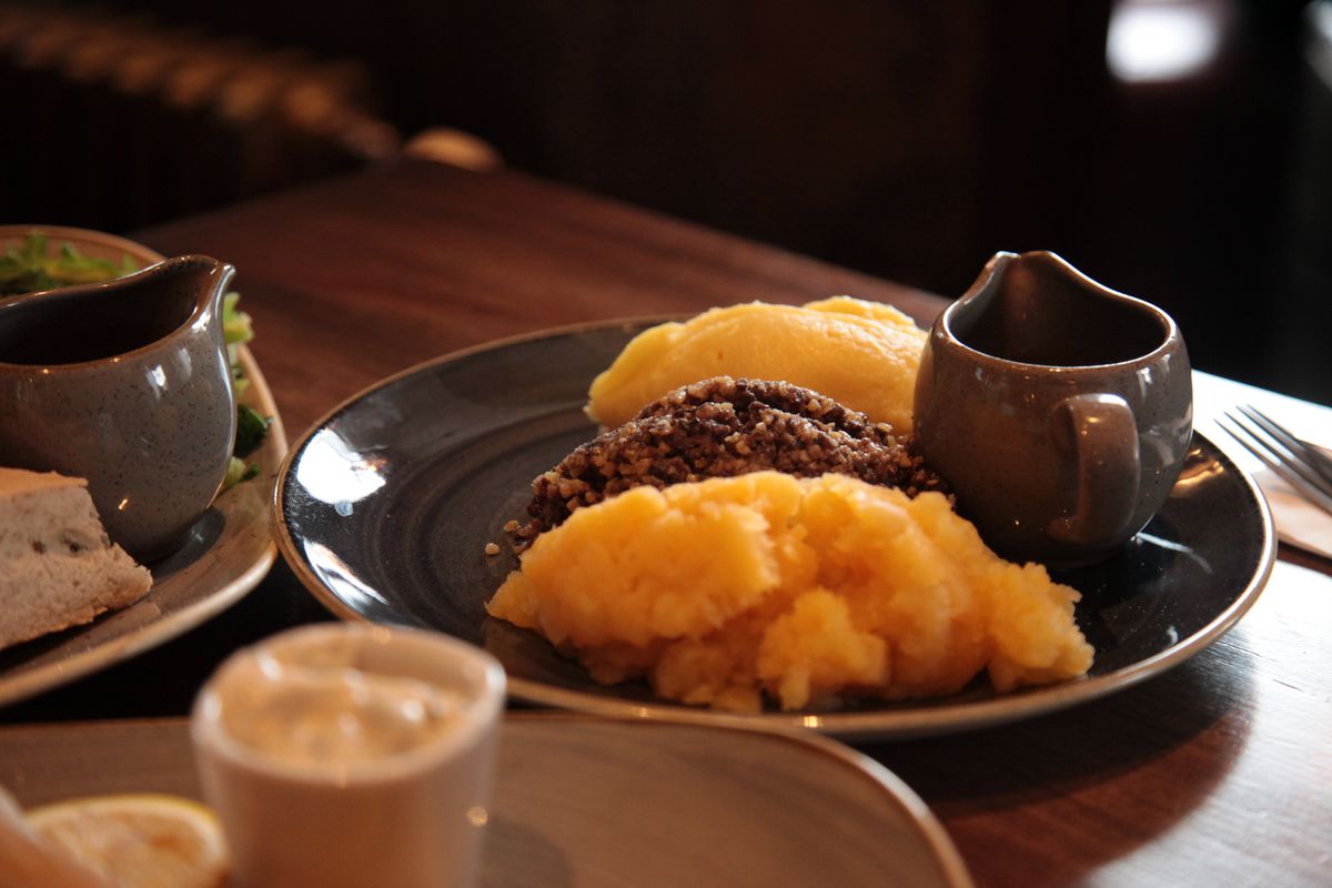 Haggis, a traditional Scottish dish made of offal, with mashed potatoes and a small gravy boat on a brown ceramic plate.