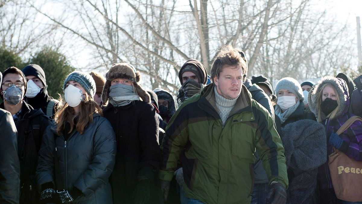 Matt Damon emerges from a crowd of people in coats and medical face masks in 2011’s Contagion.