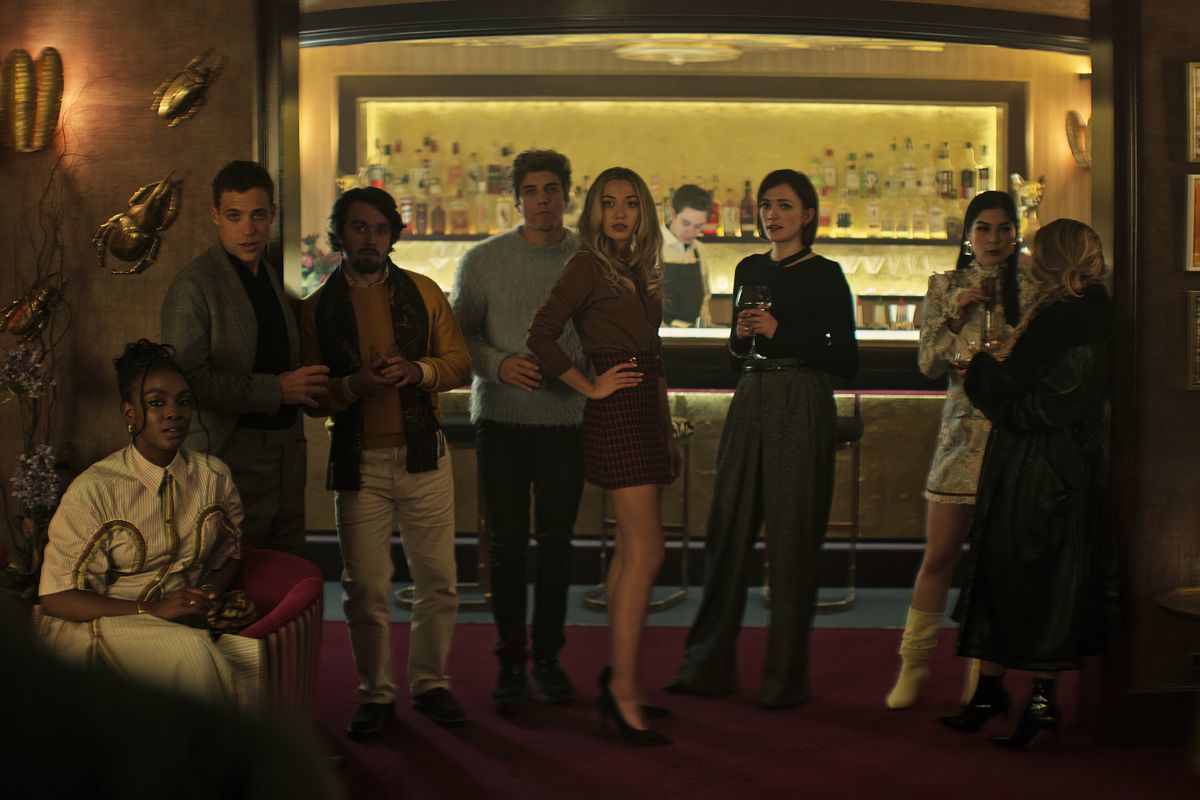 Un pequeño grupo de personas muy ricas se para frente a un bar y posa para la cámara en la temporada 4 de You de Netflix.