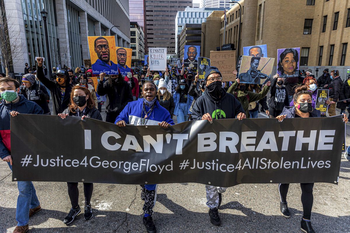 A dense, but socially distanced crowd carries paintings of George Floyd and Breonna Taylor behind a line of masked protesters who, together, are carrying a banner that reads, “I can’t breathe, justice for George Floyd, justice for all stolen lives.”