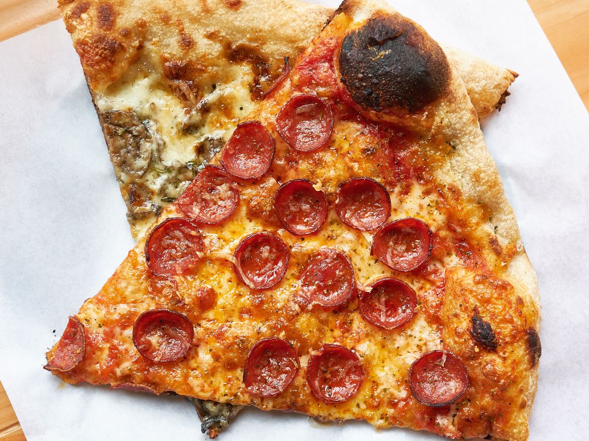 A pepperoni sliced laid on top of a mushroom pizza slice both on a sheet of wax paper.