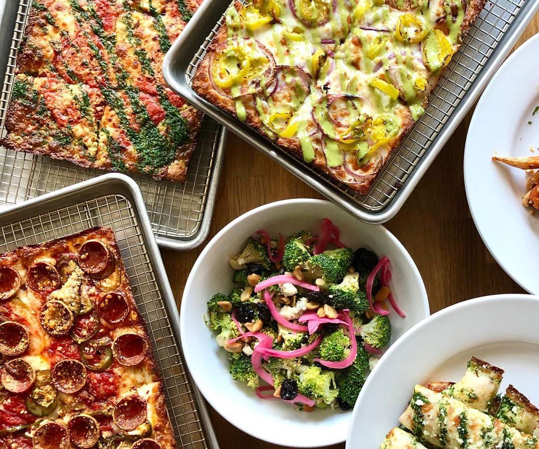 A table full of pizzas and salad from the NYC restaurant Emmy Squared. 
